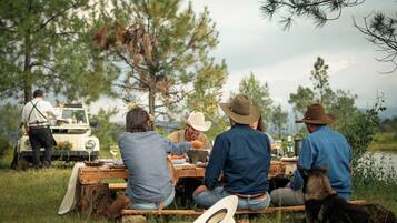 Un grupo de personas cenando al aire libre, con una mesa dispuesta para una comida, rodeadas de naturaleza.