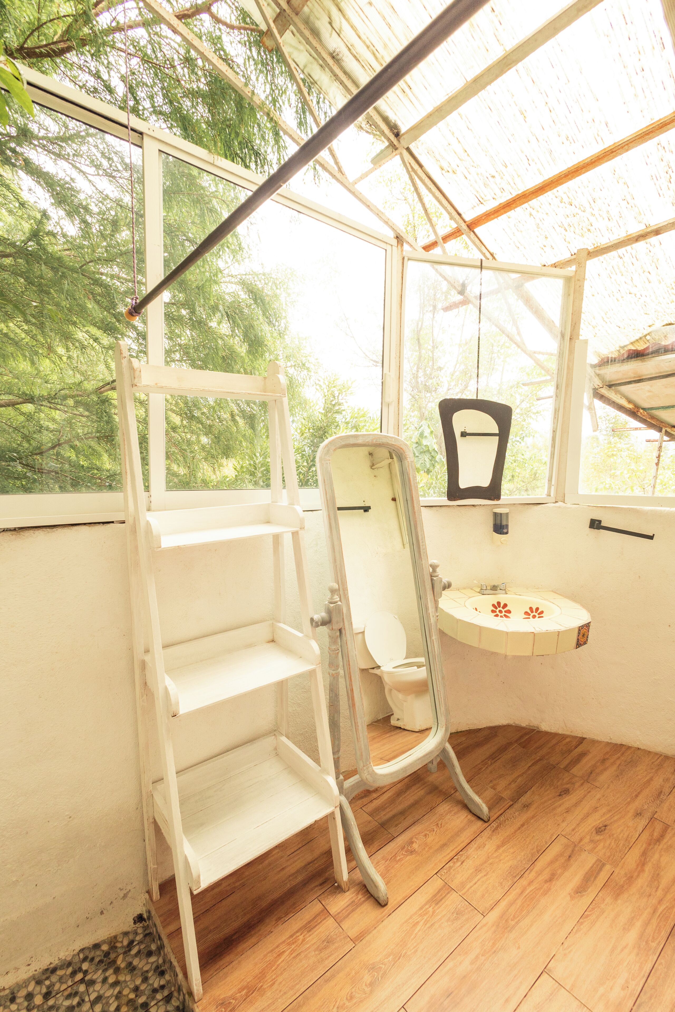 A bathroom with a wooden floor, a white sink, a mirror, and a window with a view of trees.