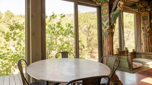 Un espace repas comprenant une table ronde et des chaises, de grandes fenêtres donnant sur la verdure et un plafond décoratif en bois.