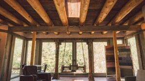 Un plafond en bois rustique agrémenté d’une lucarne, un fauteuil suspendu en bois et une fenêtre avec des rideaux.