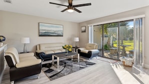 A spacious living room with a ceiling fan, a beige sofa, a black armchair, a coffee table with flowers, and a view through large glass doors to an outdoor area. - Beautiful modern townhouse with beach access and private parking (Panama City)