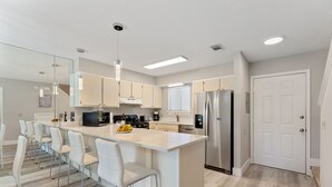 A modern kitchen with white cabinetry, a central island with bar stools, stainless steel appliances, and a large window with blinds. - Beautiful modern townhouse with beach access and private parking (Panama City)