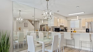 A modern kitchen with white cabinetry, a central island, and a dining area with white chairs and a glass table. - Beautiful modern townhouse with beach access and private parking (Panama City)