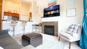 Una sala de estar moderna con chimenea, un televisor de pantalla plana y una cocina al fondo.