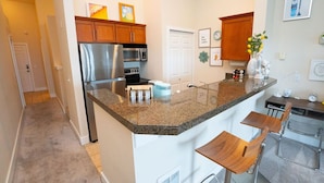 Una cocina moderna con encimera de granito, electrodomésticos de acero inoxidable, armarios de madera y una pequeña zona de bar con taburetes.