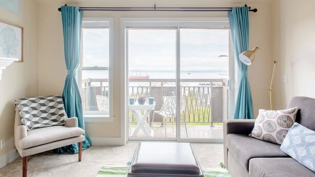 Una sala de estar con un sofá, un sillón y vista al mar a través de amplios ventanales.