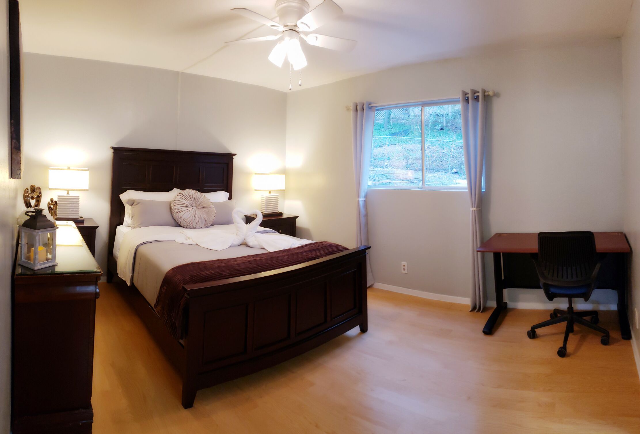 Une chambre à coucher avec un lit en bois, deux lampes de chevet, un bureau avec une chaise et une fenêtre avec des rideaux.