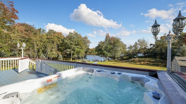 A hot tub with a wooden deck, surrounded by trees and a lake view.