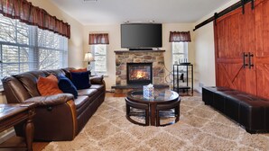 A living room with a stone fireplace, leather sofa, and a large TV.