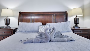 A neatly made bed with a wooden headboard, two bedside tables with lamps, and a swan-shaped towel arrangement.