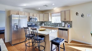 A modern kitchen with stainless steel appliances, a central island with bar stools, and a view to the dining area.