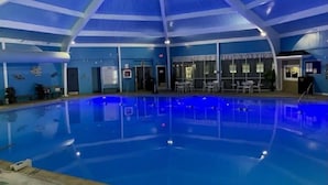 An indoor swimming pool with a blue ceiling and walls, surrounded by seating areas and a reception desk.