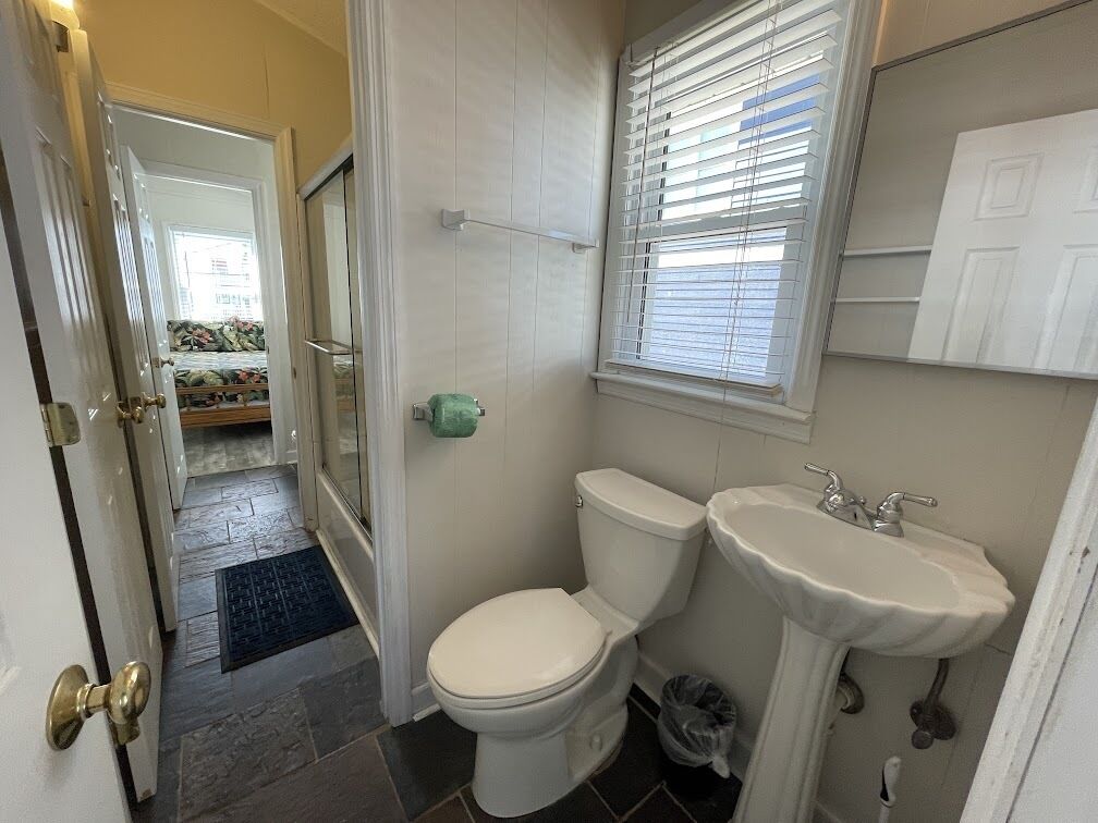A bathroom with a toilet, sink, and window with blinds.