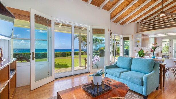 A spacious living area with a large sliding glass door leading to a balcony, a blue sofa, and a wooden coffee table. - Modern Home with Hot Tub, AC & Ocean Views! (Po'ipu)