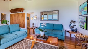 A living room with two teal sofas, a wooden coffee table, and a chessboard. - Modern Home with Hot Tub, AC & Ocean Views! (Po'ipu)