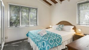 Un dormitorio con una cama, dos mesitas de noche y un ventanal con persianas.