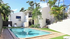 Una casa moderna de dos pisos con piscina, fachada blanca y un pequeño jardín con palmeras.