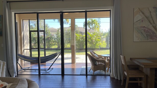A room with a large sliding glass door leading to a patio with a hammock, wicker chairs, and a dining table. - Vacation Rental Home in Bonita Springs (Bonita Springs)