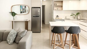 Una cocina moderna con refrigerador integrado, un comedor con taburetes de bar y una sala de estar con sofá y cojines decorativos.