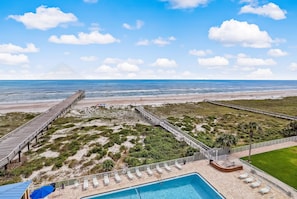 Blick auf einen Strand mit einer Holzsteganlage, einem Schwimmbecken und Liegestühlen.