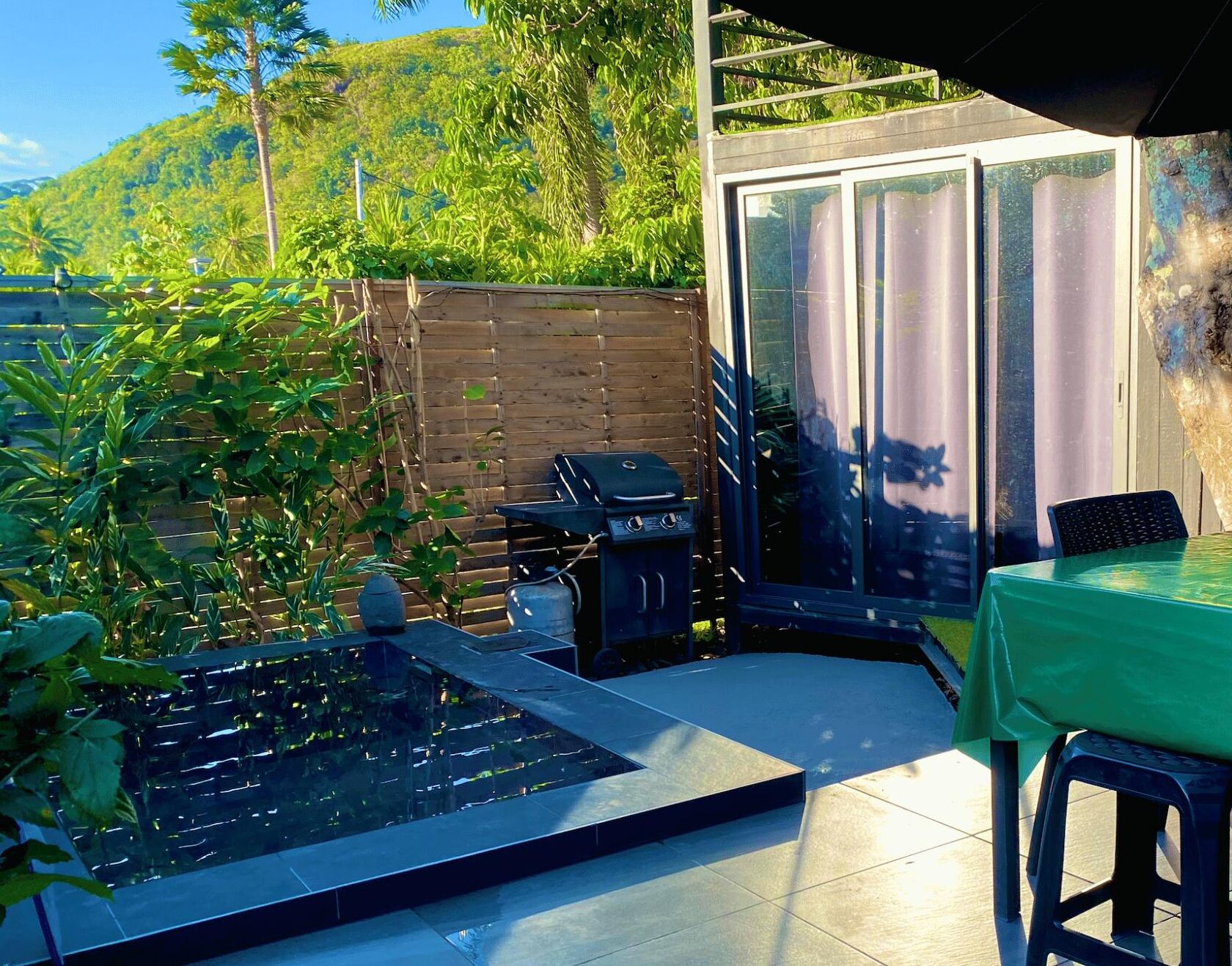 An outdoor patio with a grill, a small water feature, and a table with a green tablecloth.
