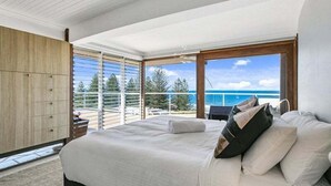 Ein Schlafzimmer mit einem großen Bett, Meerblick und einem Balkon mit Geländer.