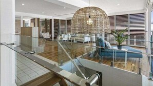 Ein geräumiges, modernes Interieur mit einer großen, gewebten Leuchte, einer Treppe und einer Sitzecke mit einem blauen Sofa.