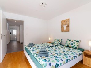 Ein Schlafzimmer mit zwei Betten, einem Holz-Kopfteil, einer an der Wand befestigten Dekoration mit einem Hirschschädel und einem zur anderen Zimmer führenden Flur.
