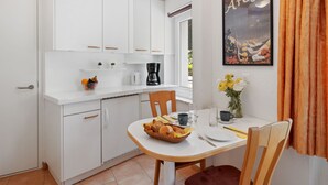 Cocina compacta con armarios blancos, cafetera y una mesa de comedor preparada para dos.