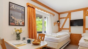 Un dormitorio con una cama, un televisor, una ventana con cortinas, una mesa con cosas para el desayuno y un cartel en la pared.