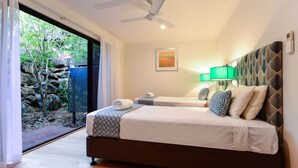 Una camera da letto con due letti, una ventola a soffitto, un comodino, una lampada e vista su un giardino tramite una porta scorrevole.