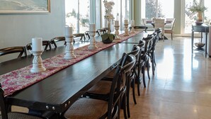 A long dining table with chairs, hanging pendant lights, and a view of the outdoors through large windows. - Sunset Manor: Luxury Wine Country Estate; Pool, Views, Steps to Wilson Creek (Temecula)