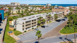 Un hotel a più piani con parcheggio, circondato da palme e vista sull'oceano.