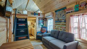 A cozy cabin interior with a wooden interior, a sofa, a table, and a ladder with signs.