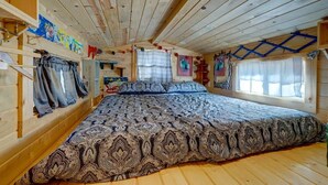 A wooden cabin bedroom with a large bed, wooden walls, and a sloped ceiling. - Cozy & rustic Tiny House in Downtown Leadville (Leadville)