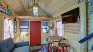 A cozy cabin interior with a red door, wooden walls, a sofa, a table with stools, and a mounted television. - Cozy & rustic Tiny House in Downtown Leadville (Leadville)