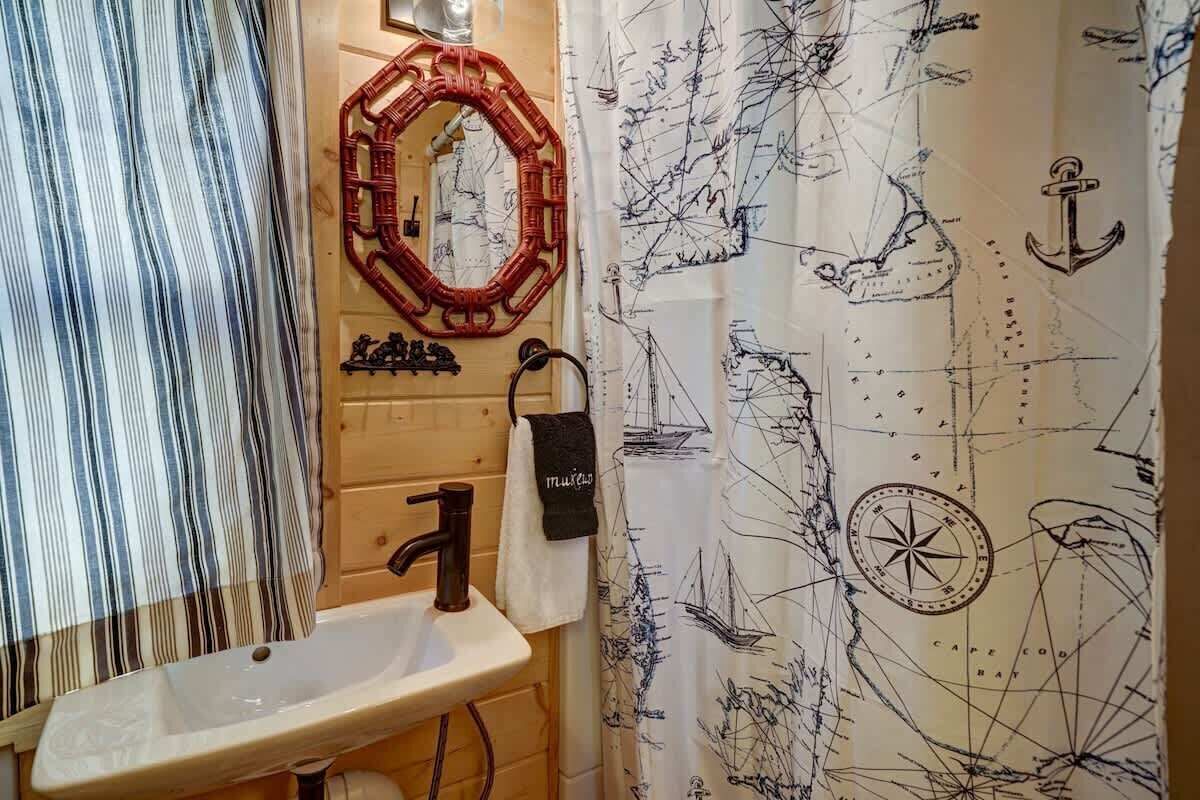 Une salle de bain avec un meuble-lavabo en bois, un lavabo blanc, un miroir et un rideau de douche sur le thème de la marine.