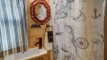 Une salle de bain avec un meuble-lavabo en bois, un lavabo blanc, un miroir et un rideau de douche sur le thème de la marine.