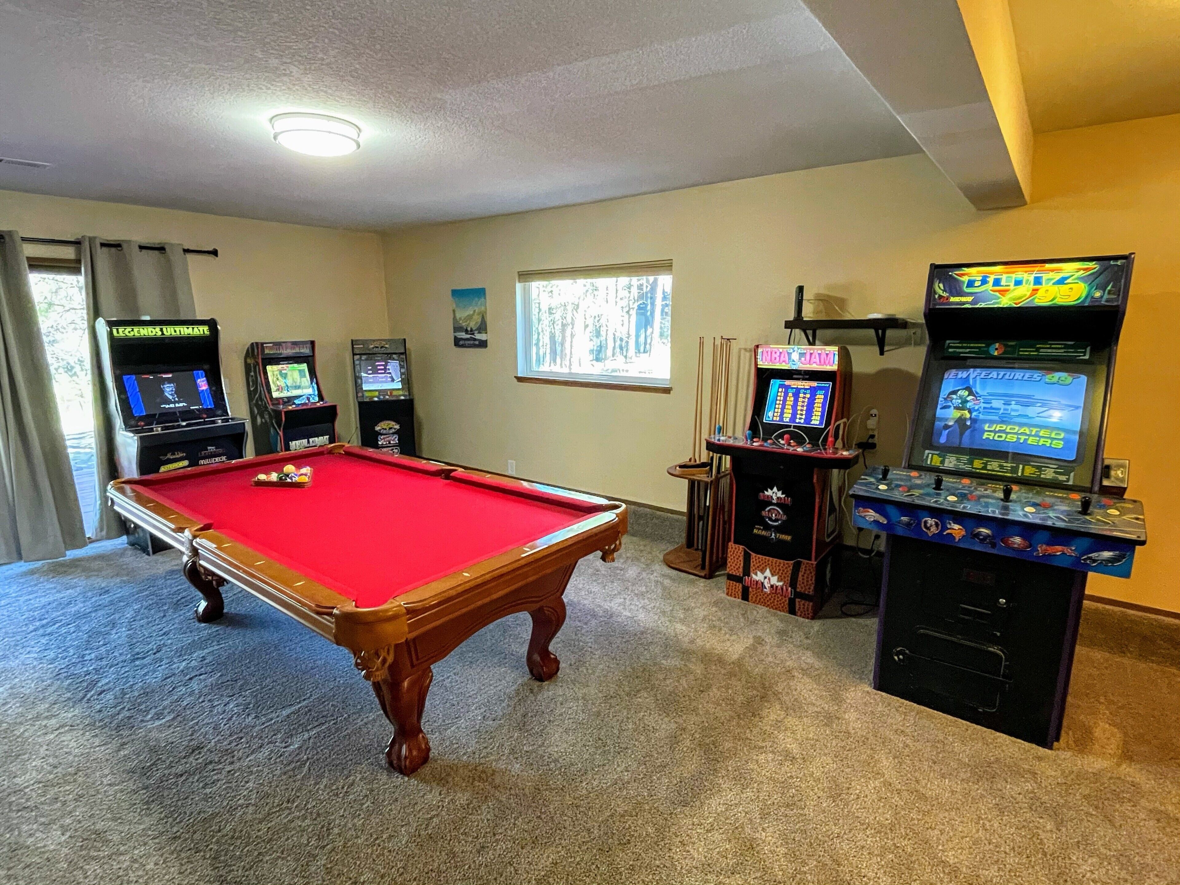A pool table in a room with arcade games and a projector screen.