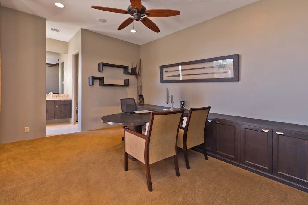 A dining area with a dark wood table, beige chairs, and a ceiling fan.
