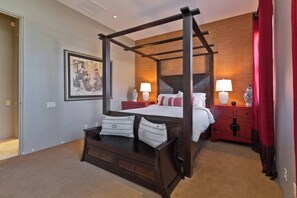 A four-poster bed with a wooden frame, a nightstand with a lamp, a red dresser, and a framed picture on the wall. - New! Stunning Modern Desert Retreat (Bermuda Dunes)