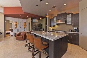 A modern kitchen with a central island, bar stools, dark cabinetry, and pendant lighting.