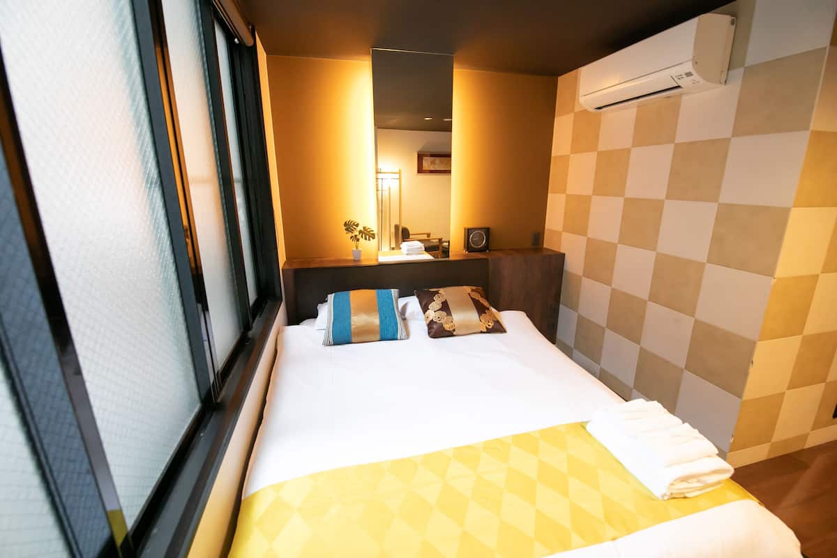 Ein Hotelzimmer mit einem Bett, einem Fenster, einem Spiegel, einer Wand-Klimaanlage und einem karierten Wandmuster.