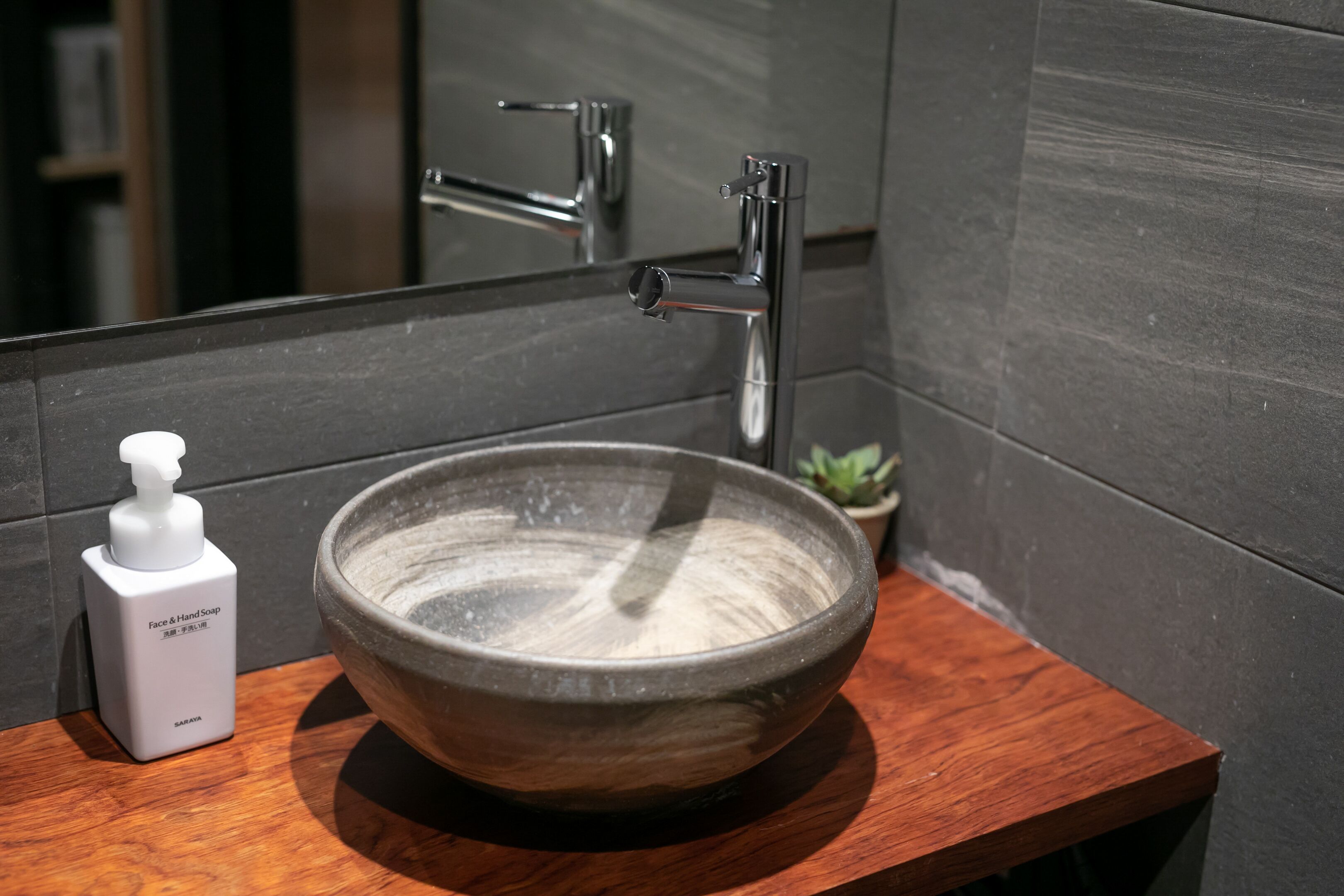 A bathroom with a wooden vanity, a large ceramic sink, and a hand soap dispenser.