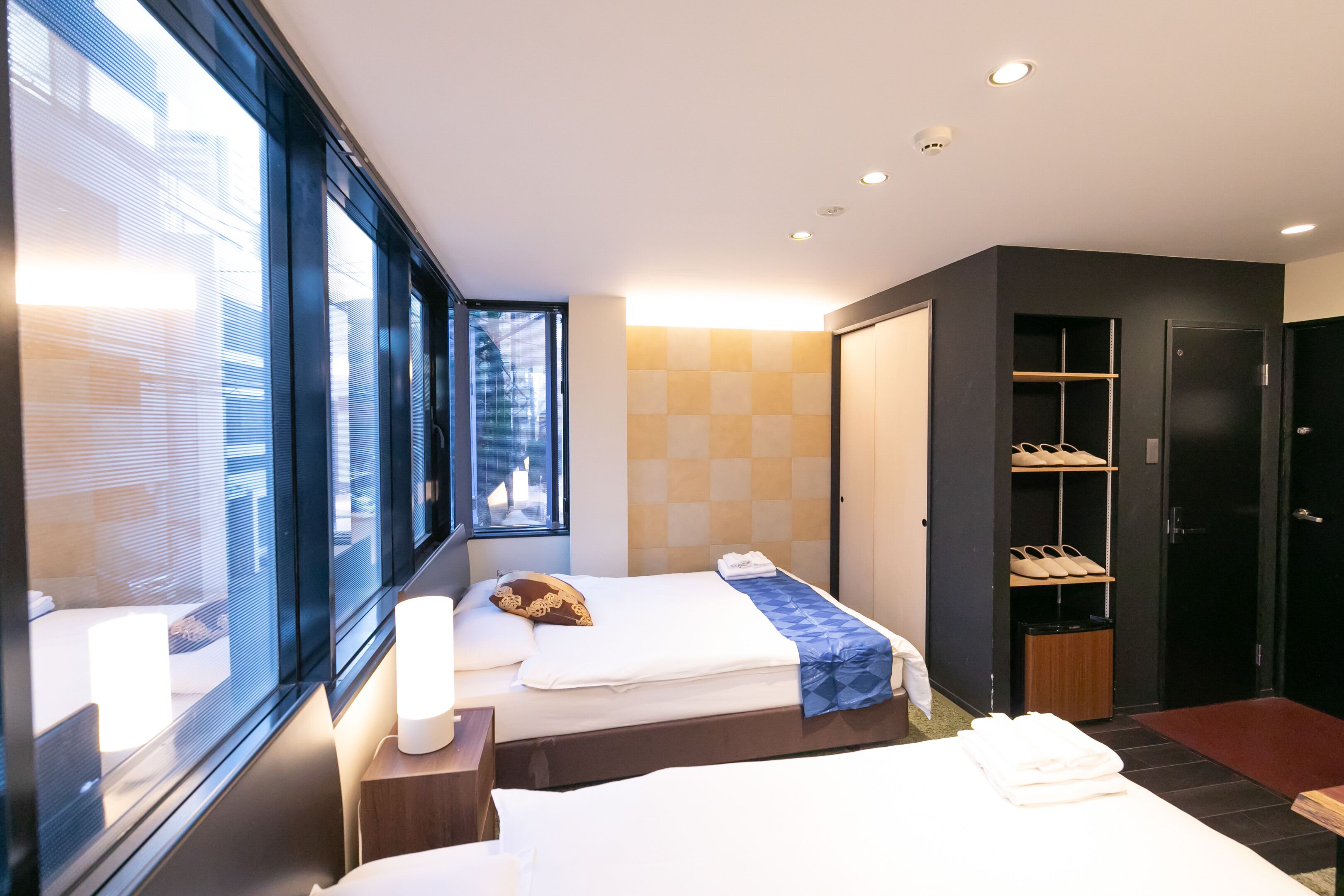 Une chambre d’hôtel moderne avec deux lits, de grandes fenêtres, une armoire et un espace de rangement pour les chaussures.