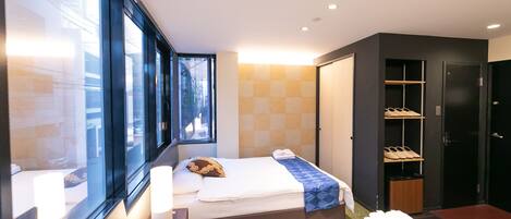 Une chambre d’hôtel moderne avec deux lits, de grandes fenêtres, une armoire et un espace de rangement pour les chaussures.