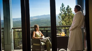 Un balcon avec vue sur les montagnes, une table avec une boisson et deux personnes.