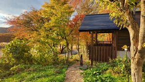 A wooden cabin with a sloped roof, surrounded by a garden with various trees and a gravel path leading to it. - A high-quality plateau life like your own home ... A natural hot spring flowing, one private plateau villa (仙北市田沢湖生保内下高野)
