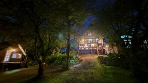 A rustic wooden building with a staircase leading up to a deck, surrounded by trees and a well-lit pathway. - A high-quality plateau life like your own home ... A natural hot spring flowing, one private plateau villa (仙北 市田沢湖生保内下高野)