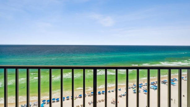 Blick auf einen Strand vom Balkon mit Geländer, Meer und Strandstühlen.